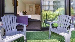 Een hotelkamer met een bed, een bank en twee stoelen. Een raam met uitzicht op een gebouw en groen.