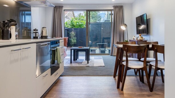 A modern kitchen with a dining area, large windows, and a flat-screen TV. - Bright and Spacious 2BR near Ara Institute and CBD (Christchurch)