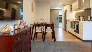 A modern kitchen with a dining area, featuring a wooden table and chairs, a built-in oven, and a large window. - Bright and Spacious 2BR near Ara Institute and CBD (Christchurch)