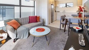 A modern living room with a grey sofa, a round coffee table, and a dining area with a table and chairs. - City Escape - Near New Brighton Beach & He Puna (Christchurch)