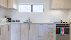 A modern kitchen with light wood cabinets, a stainless steel sink, and an oven. - City Escape - Near New Brighton Beach & He Puna (Christchurch)