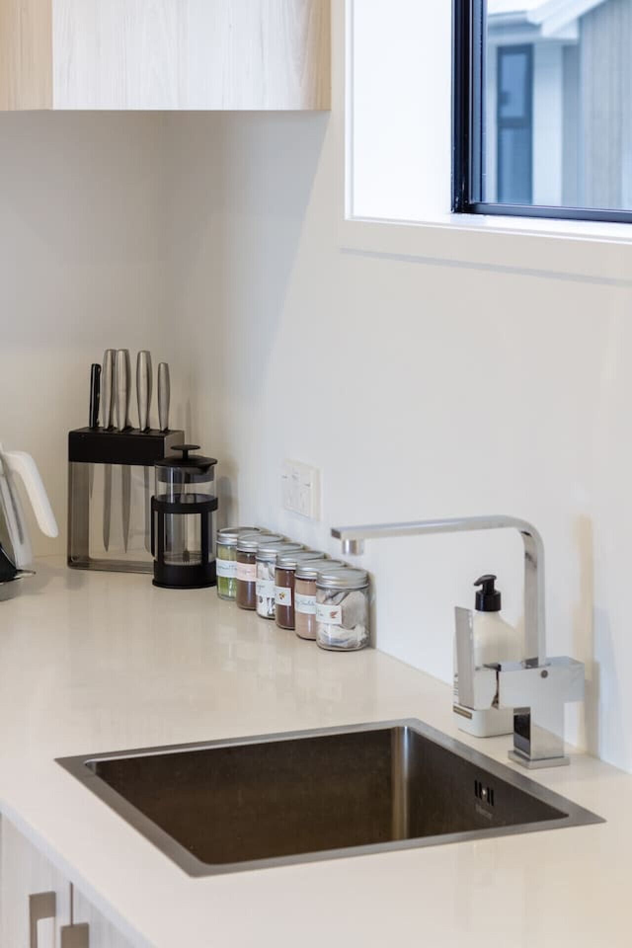 Una cocina moderna con un lavamanos de acero inoxidable, una cafetera y un bloque de cuchillos.