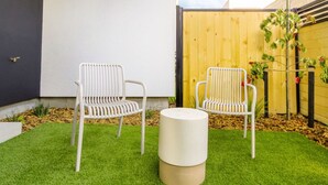 Dos sillas blancas y una mesa redonda sobre un césped verde en un jardín.