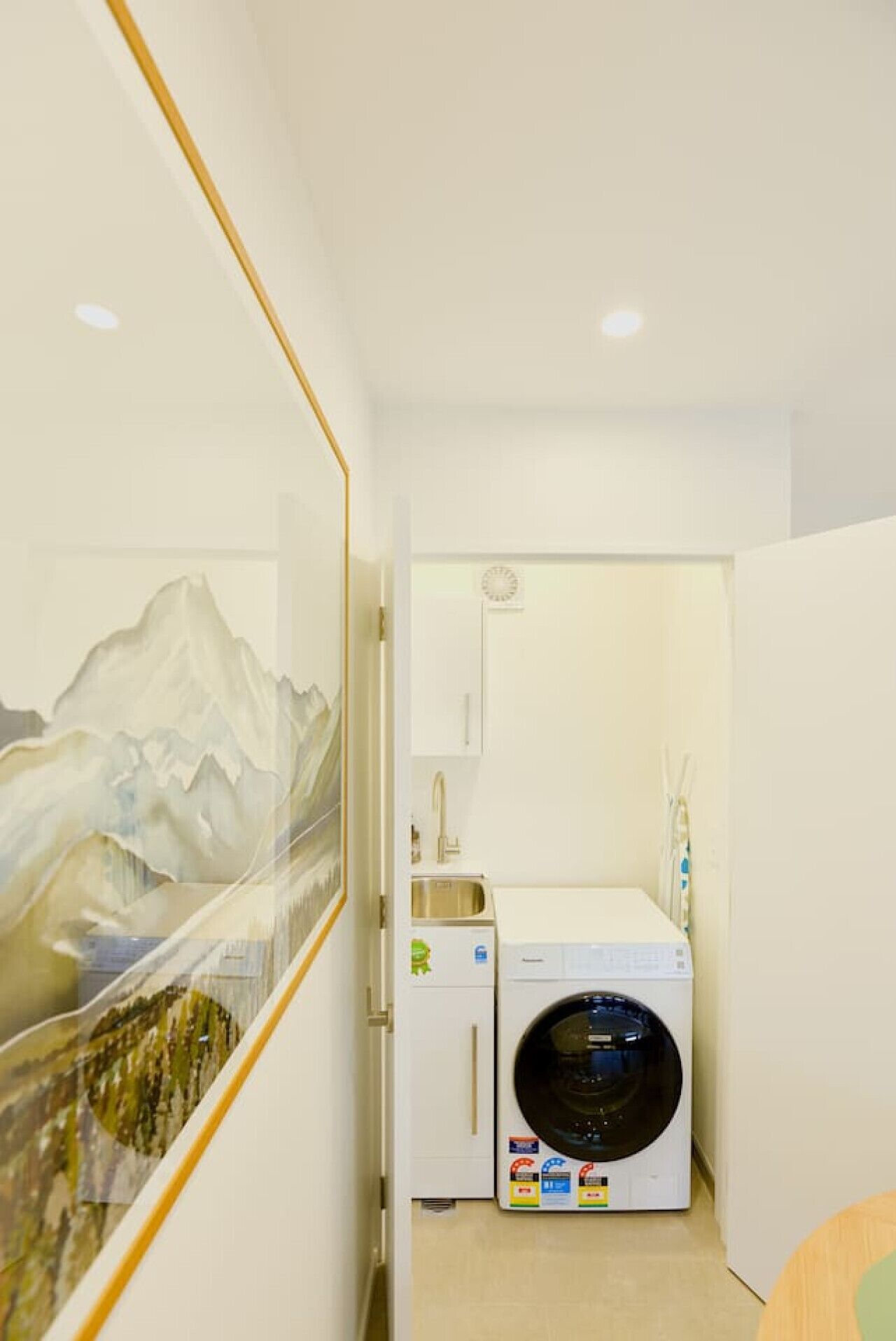 Une petite buanderie équipée d’un lave-linge, d’un évier et d’un tableau représentant des montagnes.