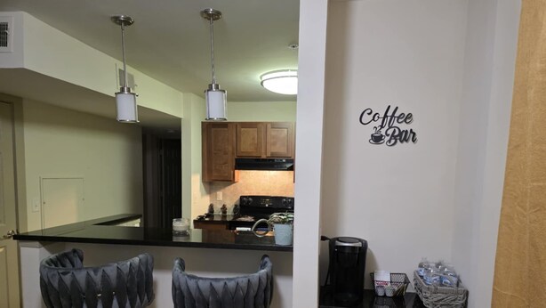 Una cocina con dos taburetes de bar, una cafetera y un cartel en la pared que dice "Coffee Bar".