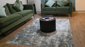 Una sala de estar con dos sofás verdes, una mesa de centro negra y un tapete estampado.