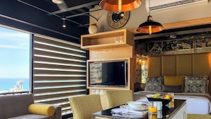 A modern hotel room with a large TV, comfortable seating, a dining area, and a view of the sea. - Suite with ocean front views in the Romantc Zone - C404 (Puerto Vallarta)