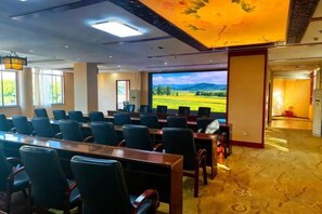 Un salón de conferencias con una pantalla grande, filas de sillas y piso alfombrado.