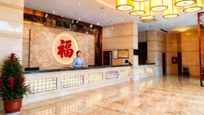 Zona de recepción de un hotel con un mostrador de mármol, una recepcionista y un cartel iluminado grande.