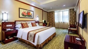 Habitación de hotel con una cama grande, un escritorio, una silla, un televisor y un cuadro en la pared.