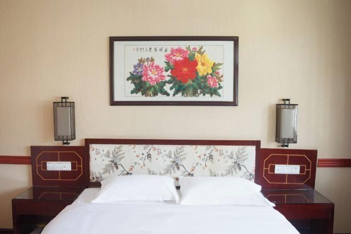 Habitación de hotel con una cama, dos mesitas de noche, cabecera con papel tapiz floral y un cuadro enmarcado de flores en la pared.