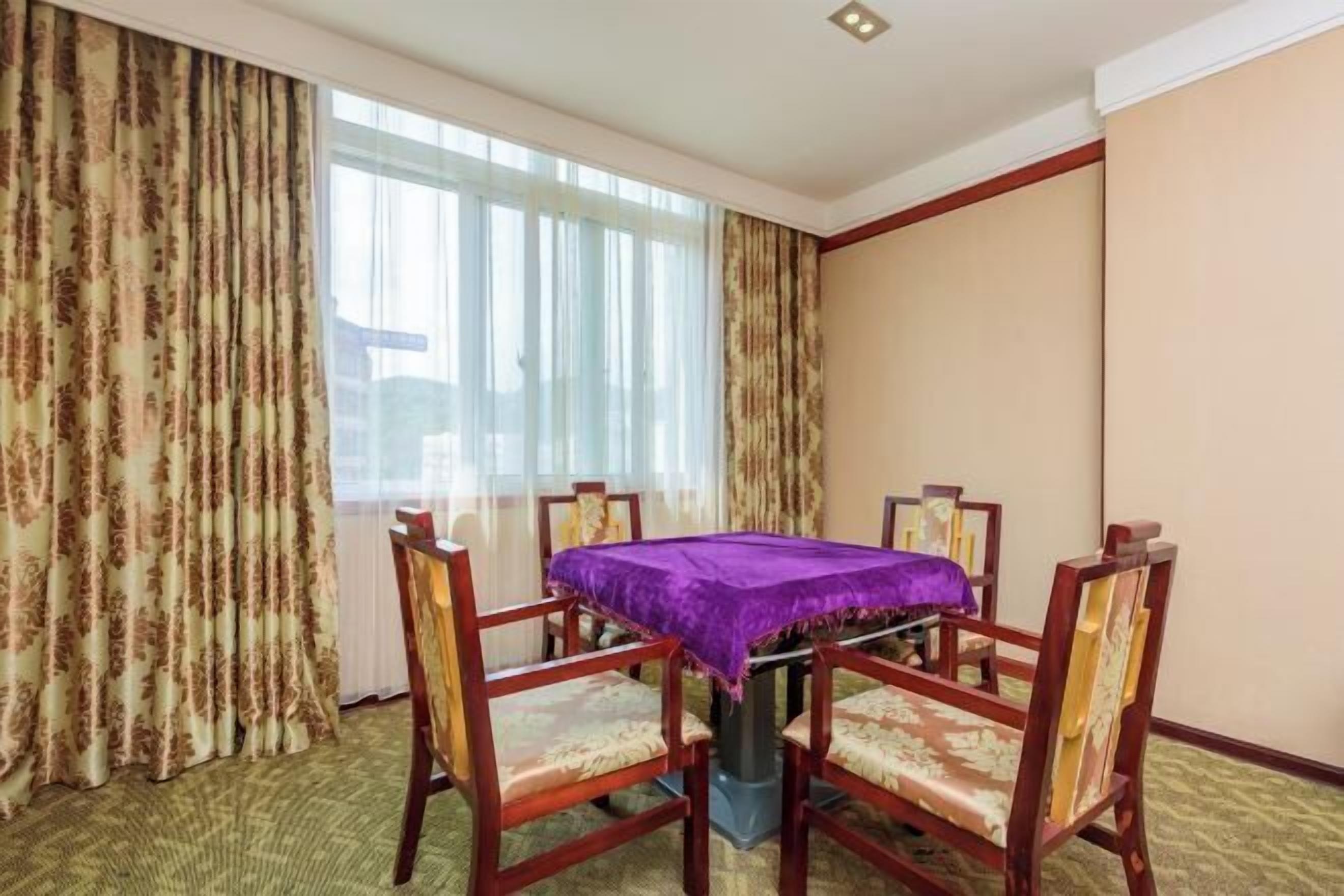 Una habitación de hotel con una mesa de comedor, cuatro sillas y un ventanal con cortinas.