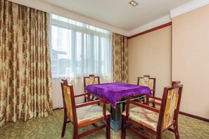 Una habitación de hotel con una mesa de comedor, cuatro sillas y un ventanal con cortinas.
