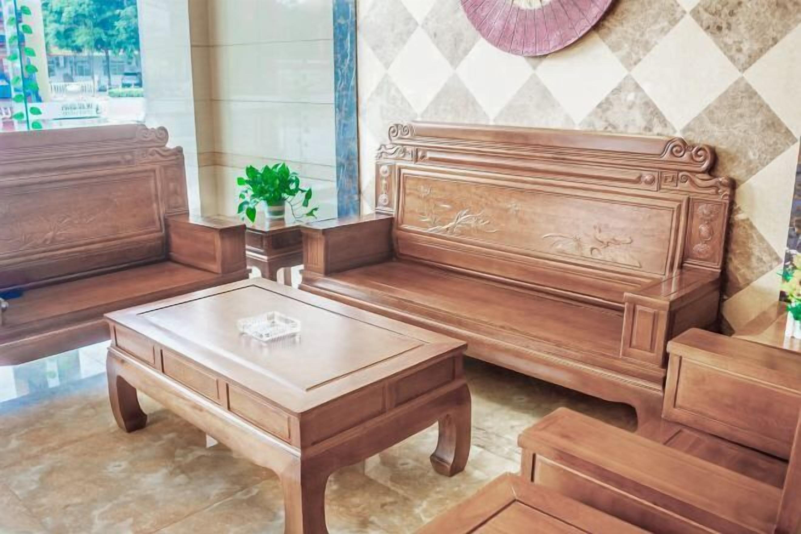 A wooden sofa set with a matching coffee table, positioned in a room with a patterned wall and a window.