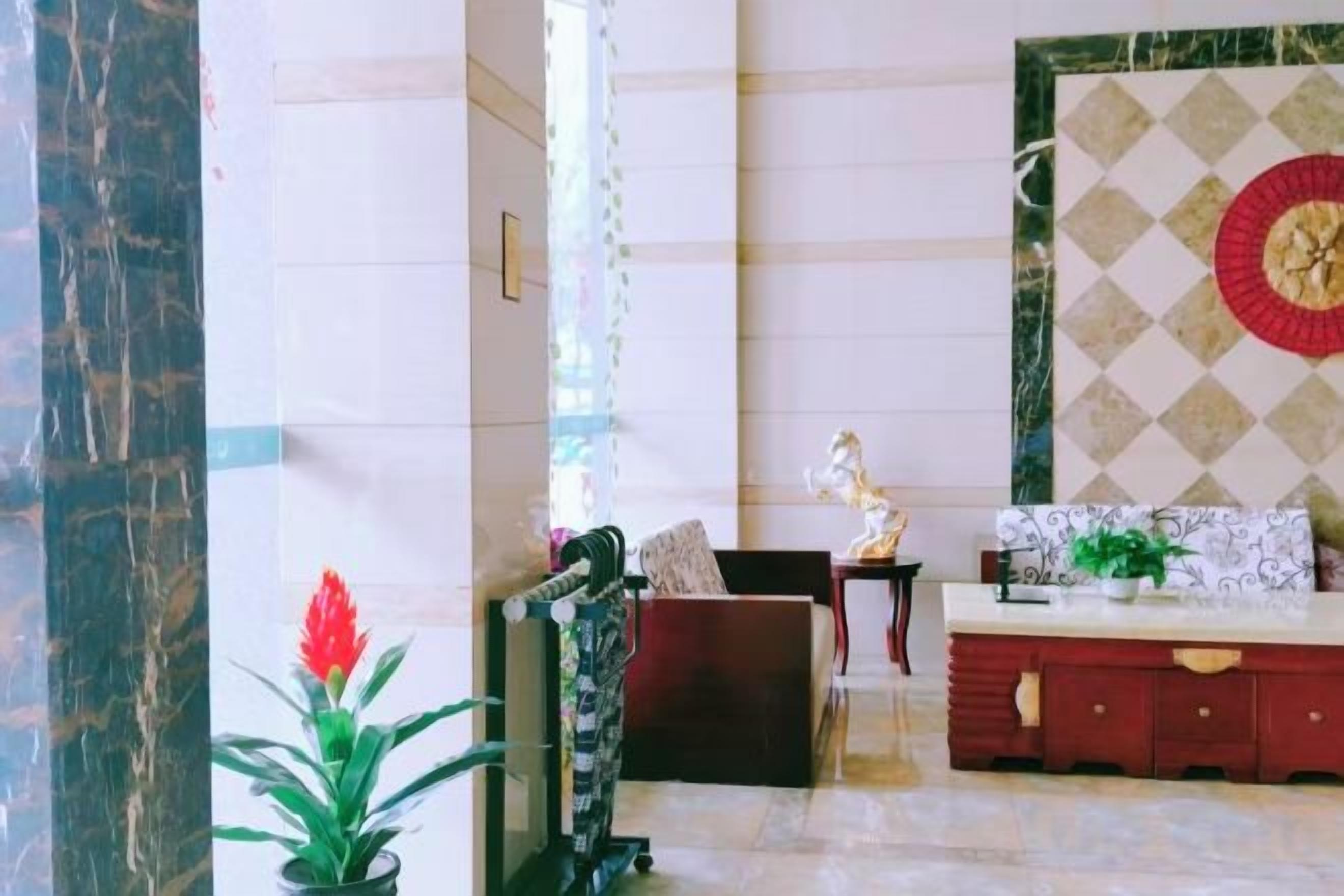 Un hall d’entrée avec une colonne en marbre, un canapé, un buffet rouge et un mur décoratif.
