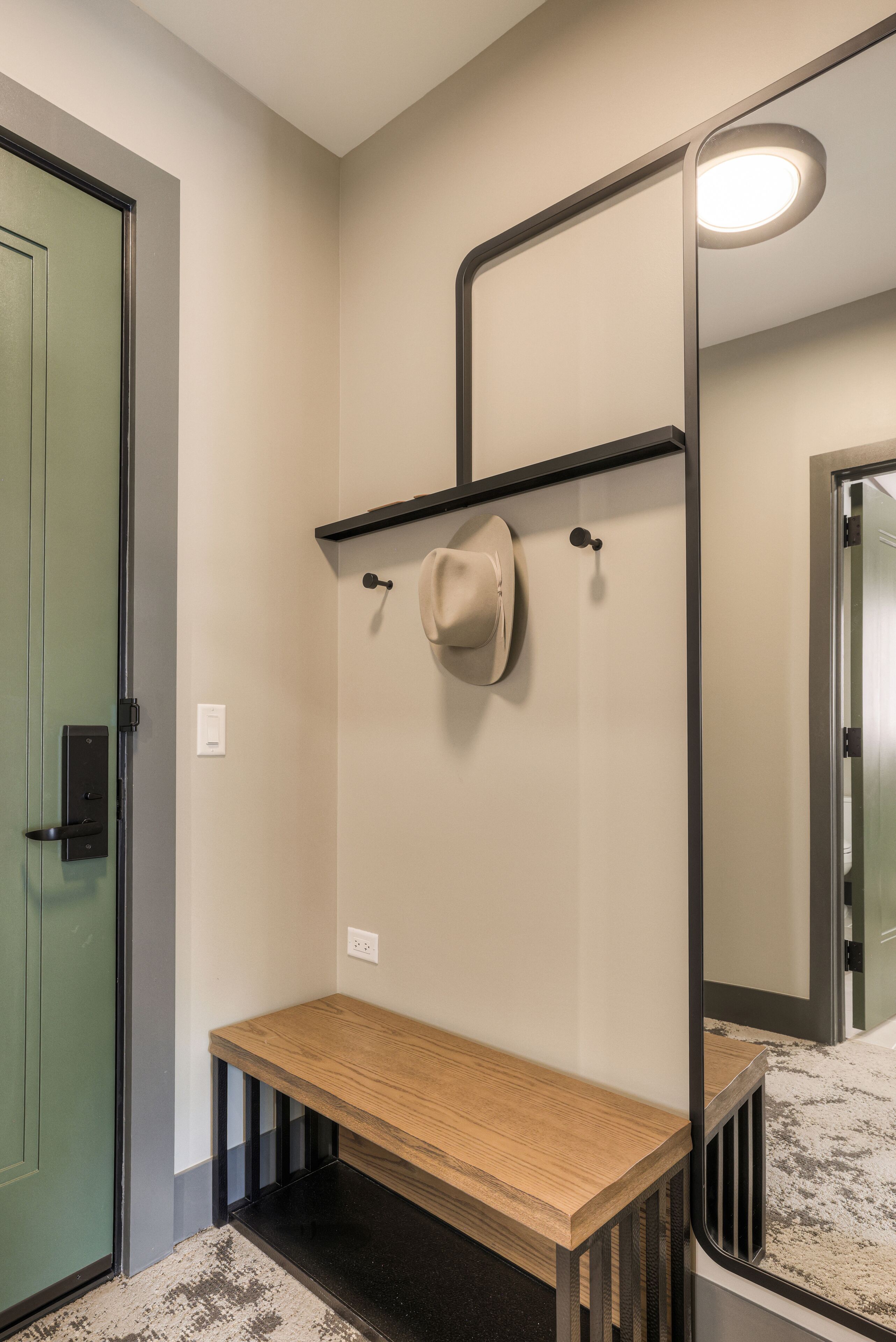 A room with a wooden bench, a mirror, a hat on a hook, and a door.
