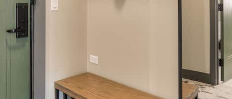 A room with a wooden bench, a mirror, a hat on a hook, and a door.