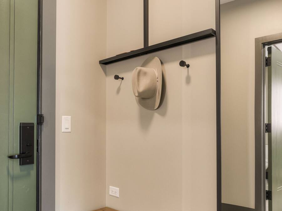 A room with a wooden bench, a mirror, a hat on a hook, and a door.