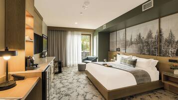 A hotel room with a bed, desk, chair, and a large window with a view of trees.