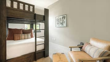Una cama litera con almohadas, un sofá, una mesita y un cuadro en la pared.
