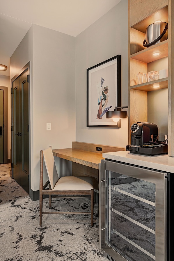 A hotel room with a desk, chair, coffee machine, framed artwork, and a shelf with kitchenware. - Kindred Resort a RockResort (Keystone)