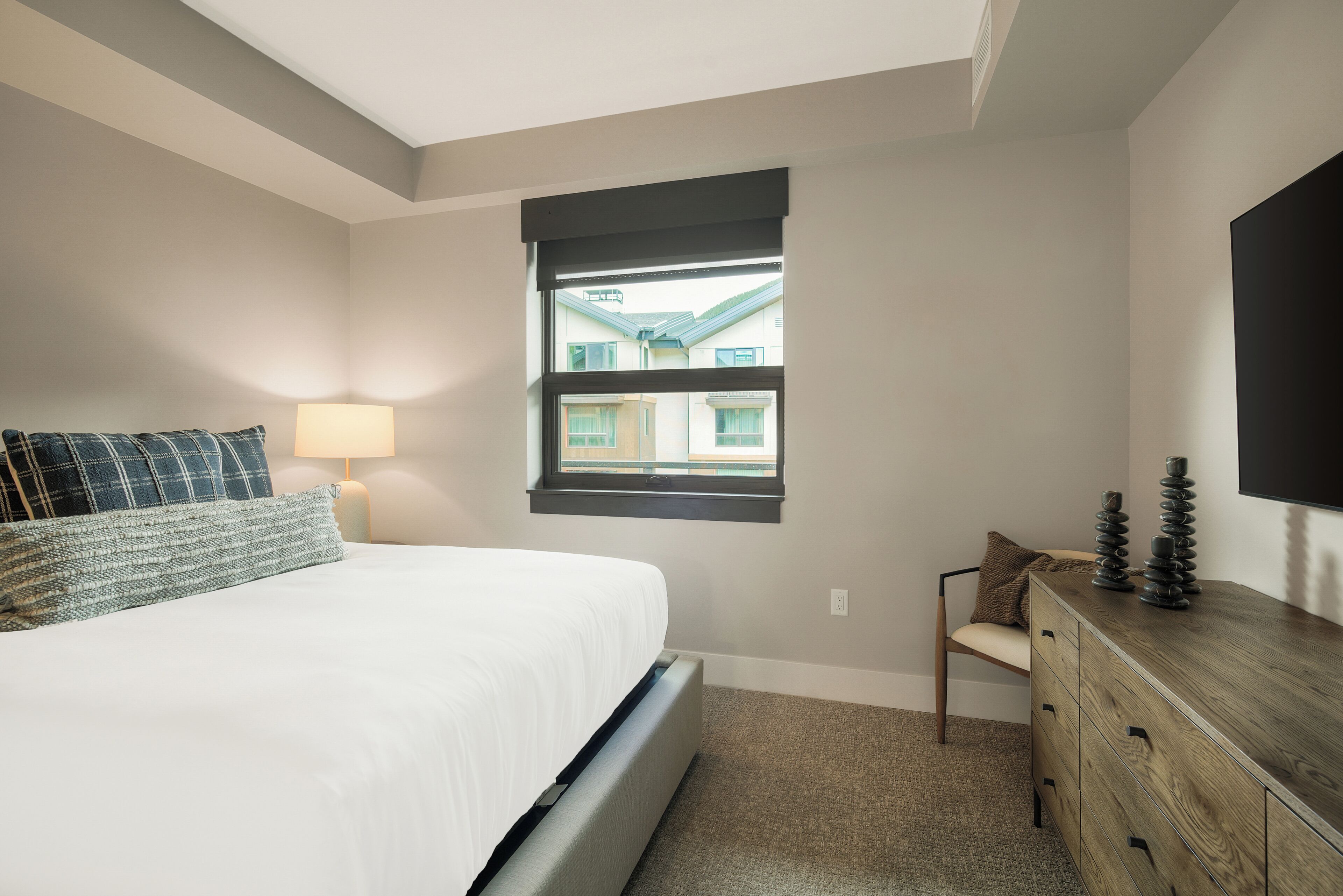 A bedroom with a bed, a window, a dresser, and a lamp.