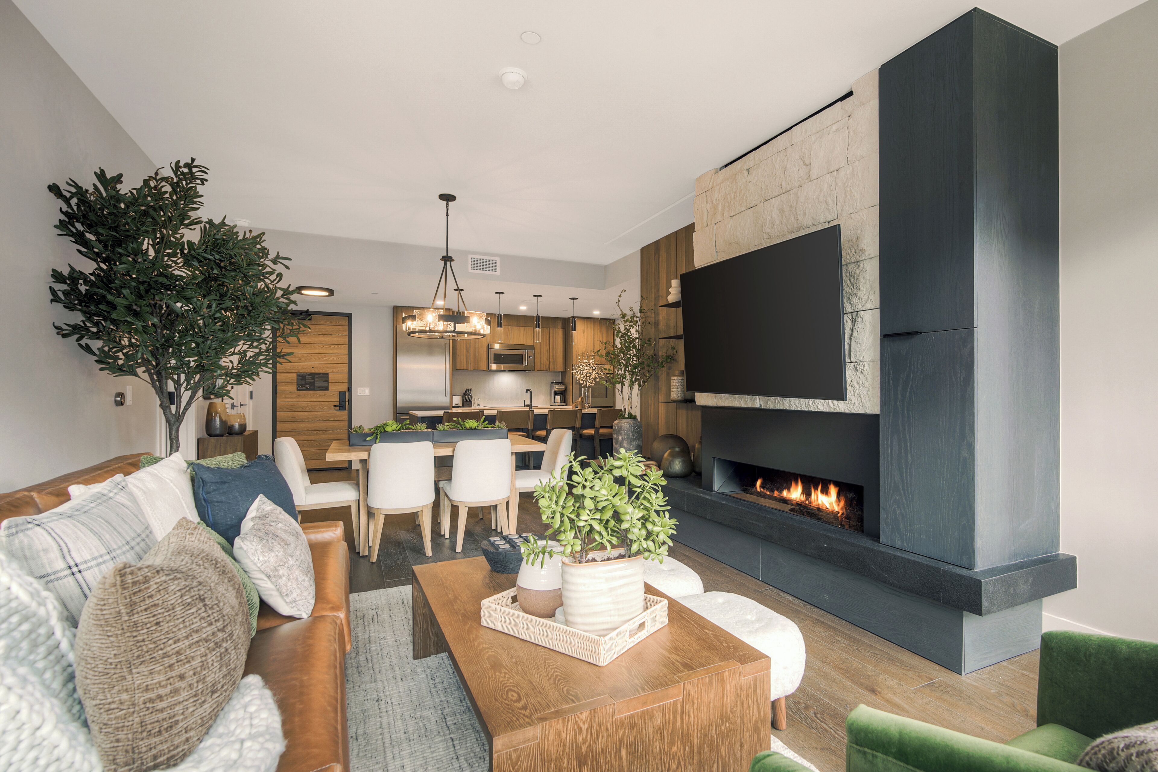 A modern living room with a fireplace, a dining area, and a kitchen in the background.