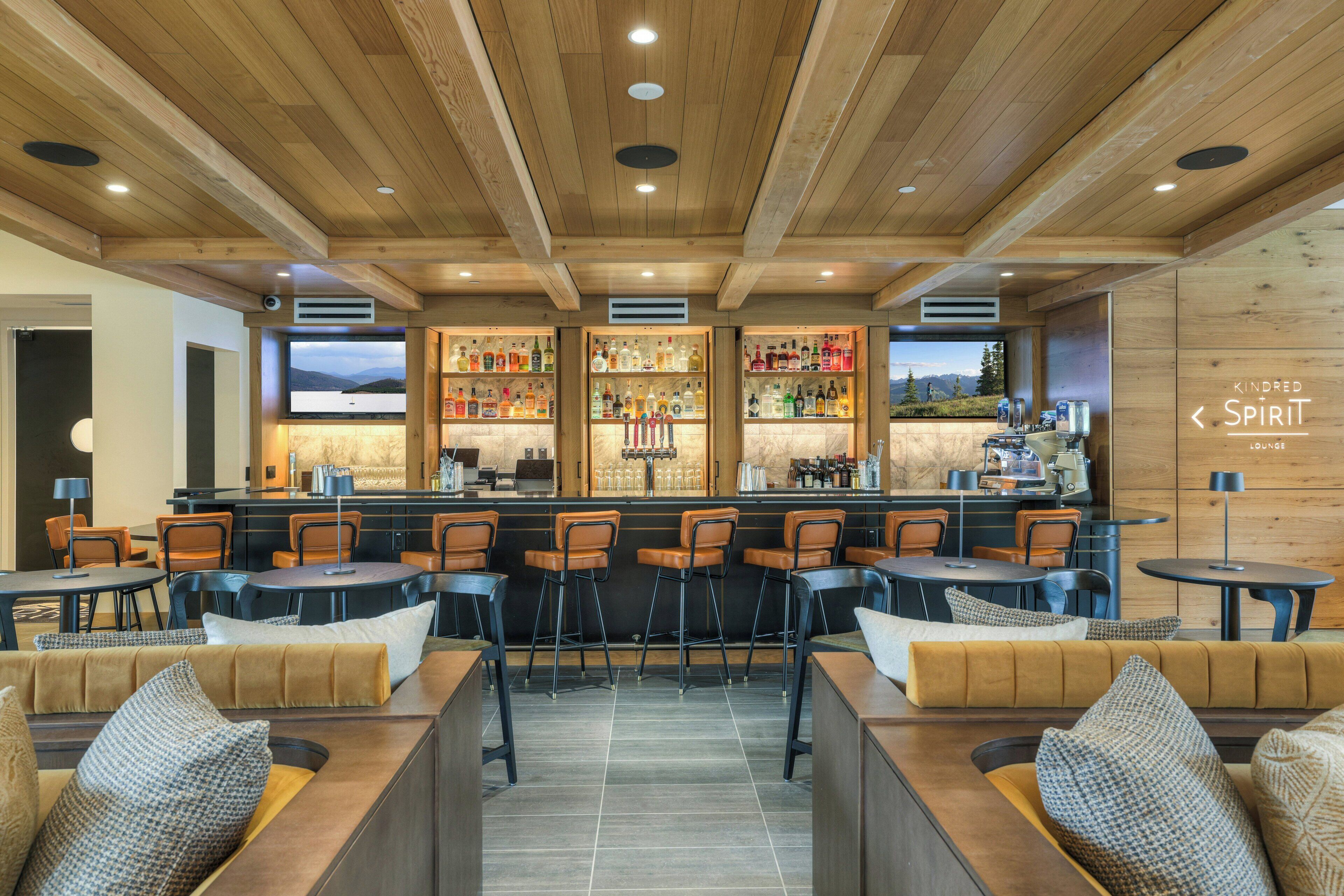 A bar area with wooden ceiling, bar stools, and a bar counter with bottles.