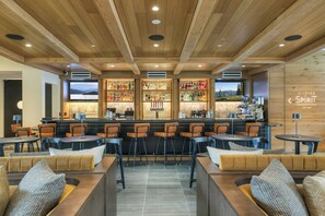 A bar area with wooden ceiling, bar stools, and a bar counter with bottles.