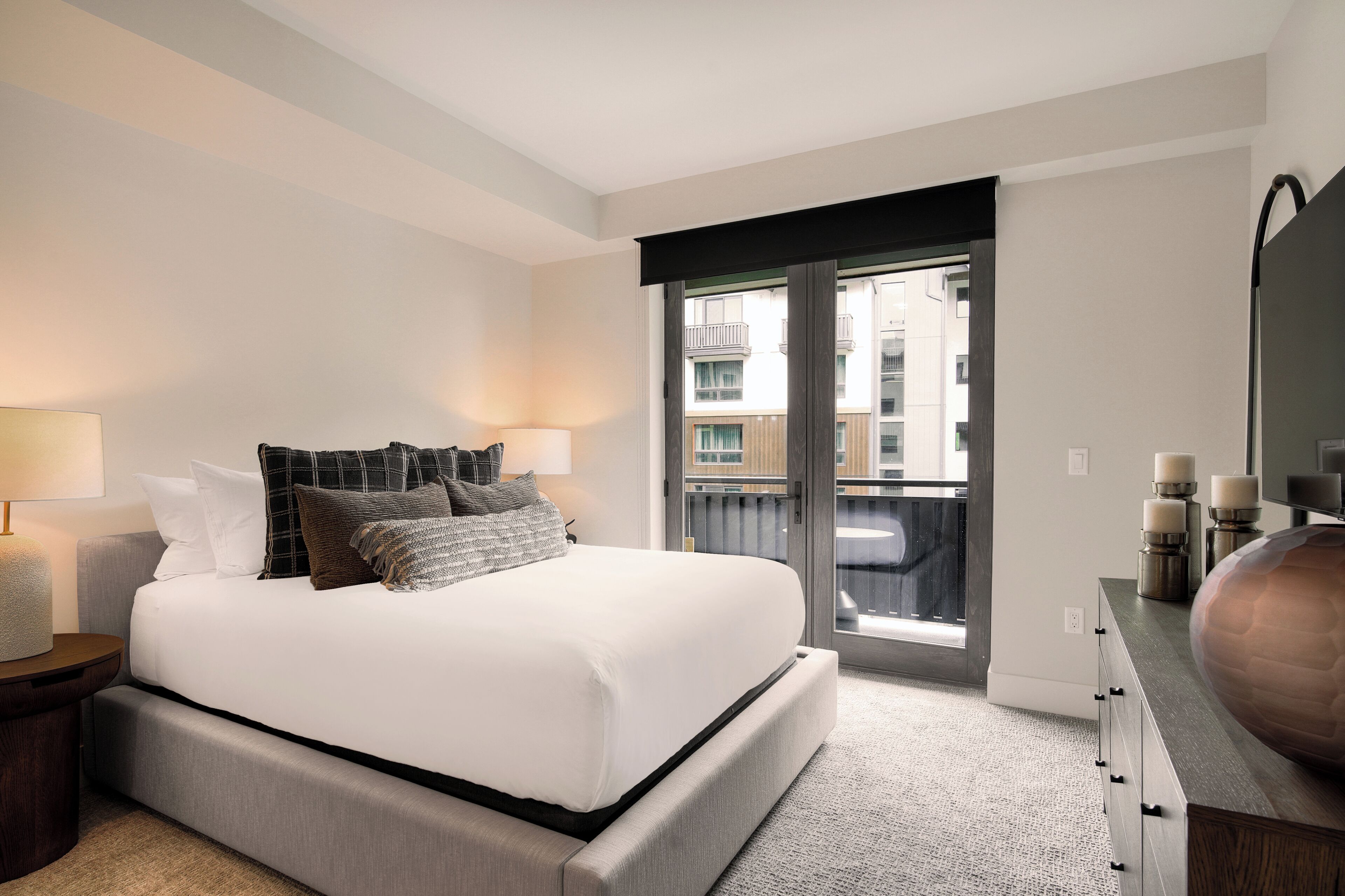 Habitación de hotel moderna con una cama grande, dos lámparas de noche, vistas al balcón exterior y un espejo grande en la pared.