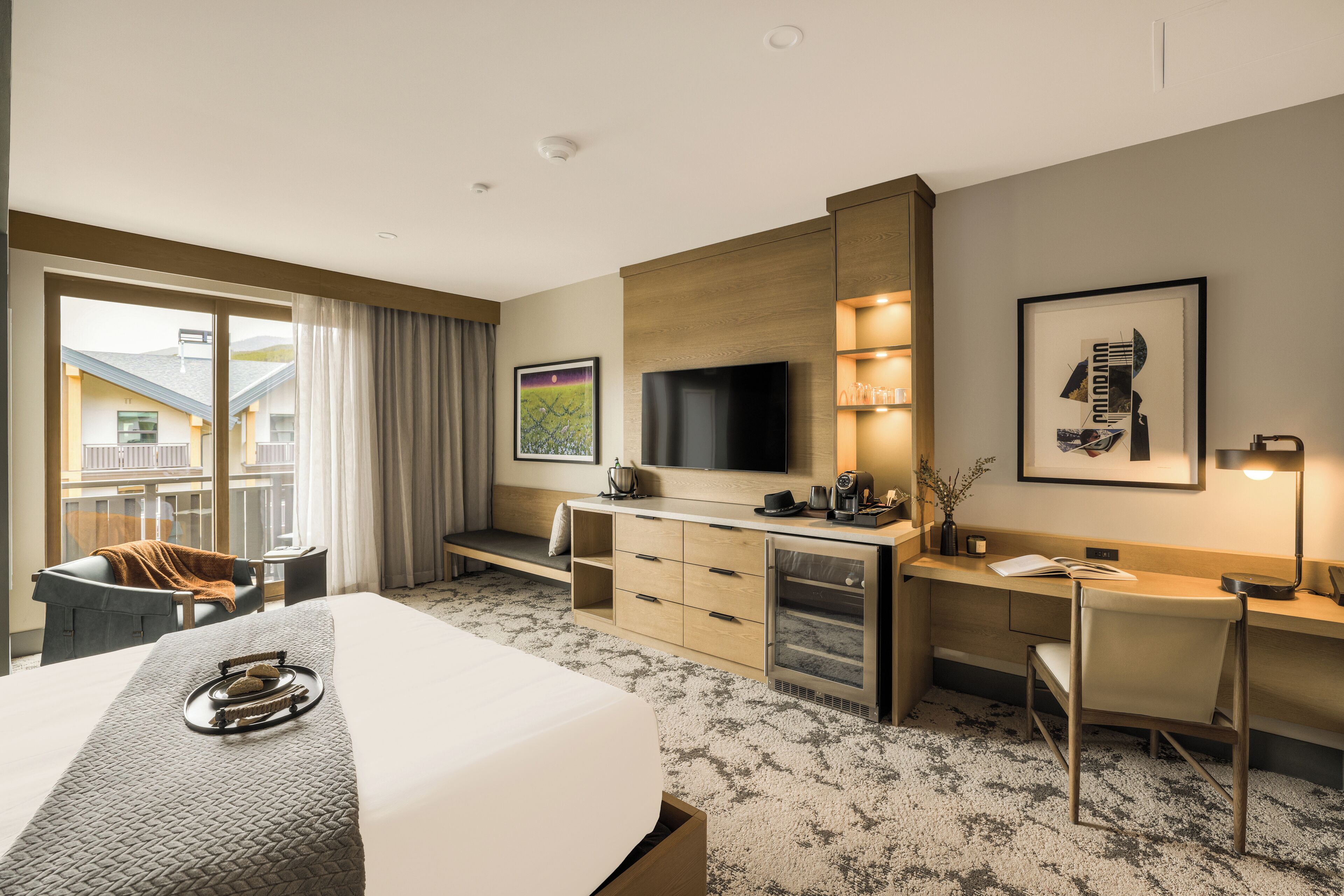 Ein Hotelzimmer mit Bett, Schreibtisch, Fernseher und Blick auf Gebäude.