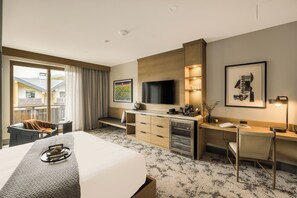A hotel room with a bed, desk, TV, and a view of buildings outside. - Kindred Resort a RockResort (Keystone)