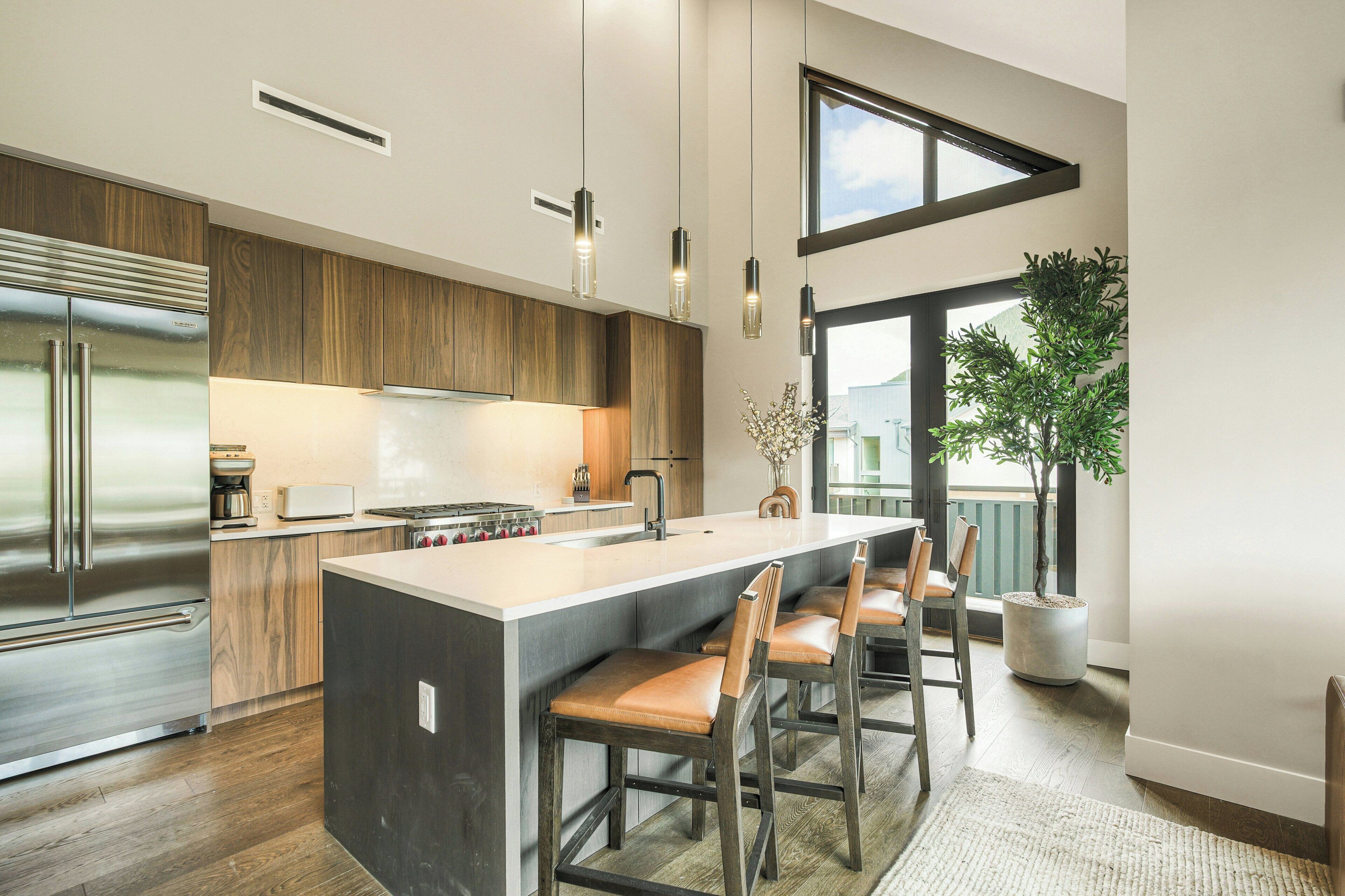 Une cuisine moderne dotée d’un grand îlot central, d’appareils électroménagers en acier inoxydable et de meubles de rangement en bois.