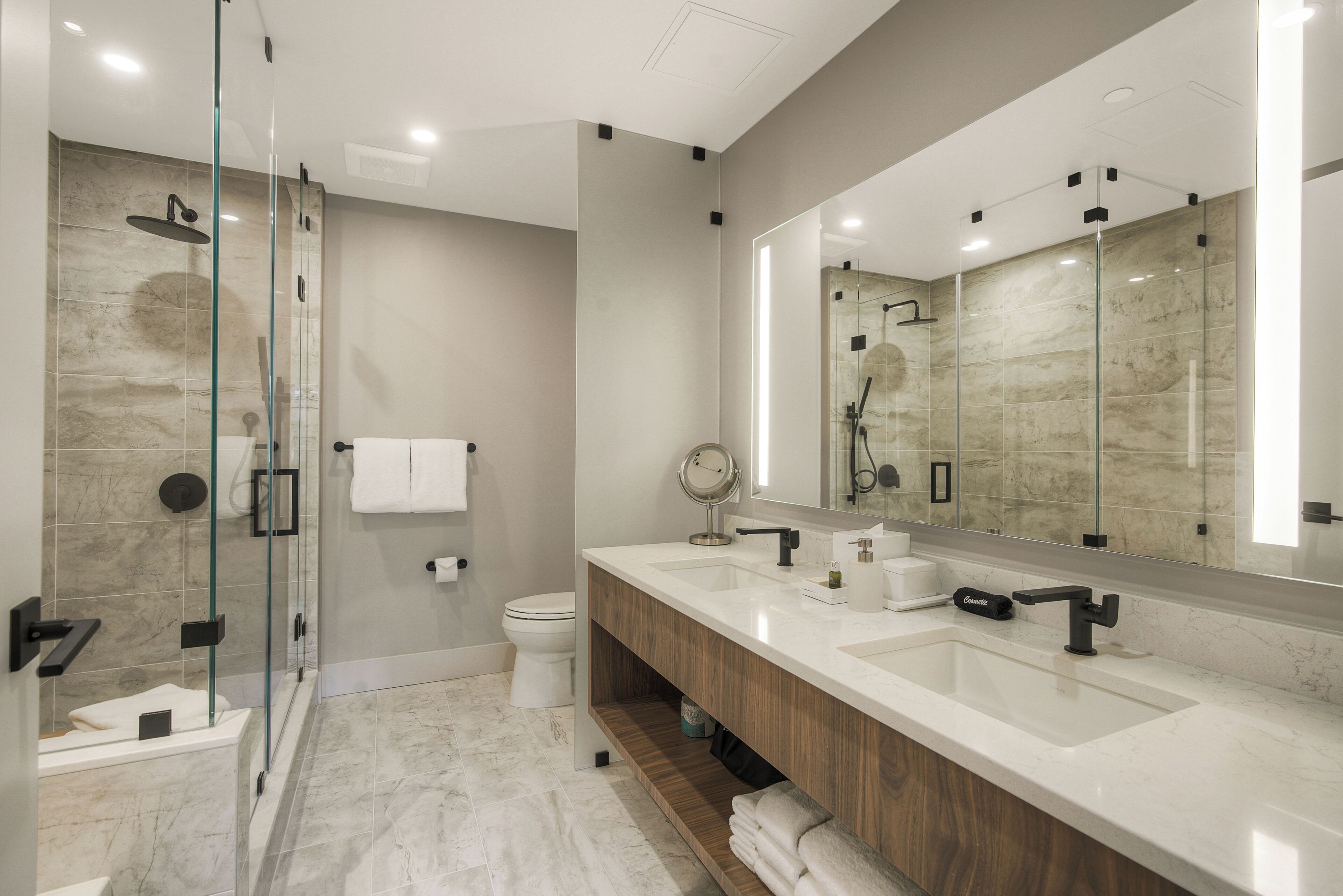 Une salle de bain moderne avec une douche à parois de verre, un meuble-lavabo à deux vasques et un grand miroir.