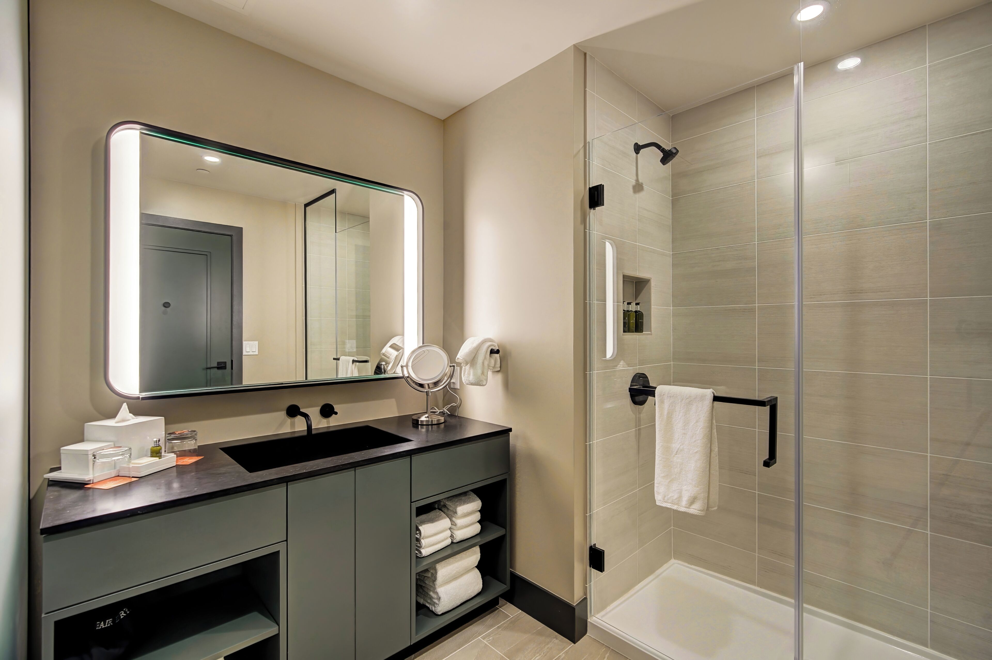 A modern bathroom with a glass-enclosed shower, a large mirror, and a vanity with a sink and towel storage.