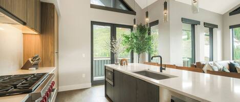 A modern kitchen with a large island, stainless steel appliances, and large windows.