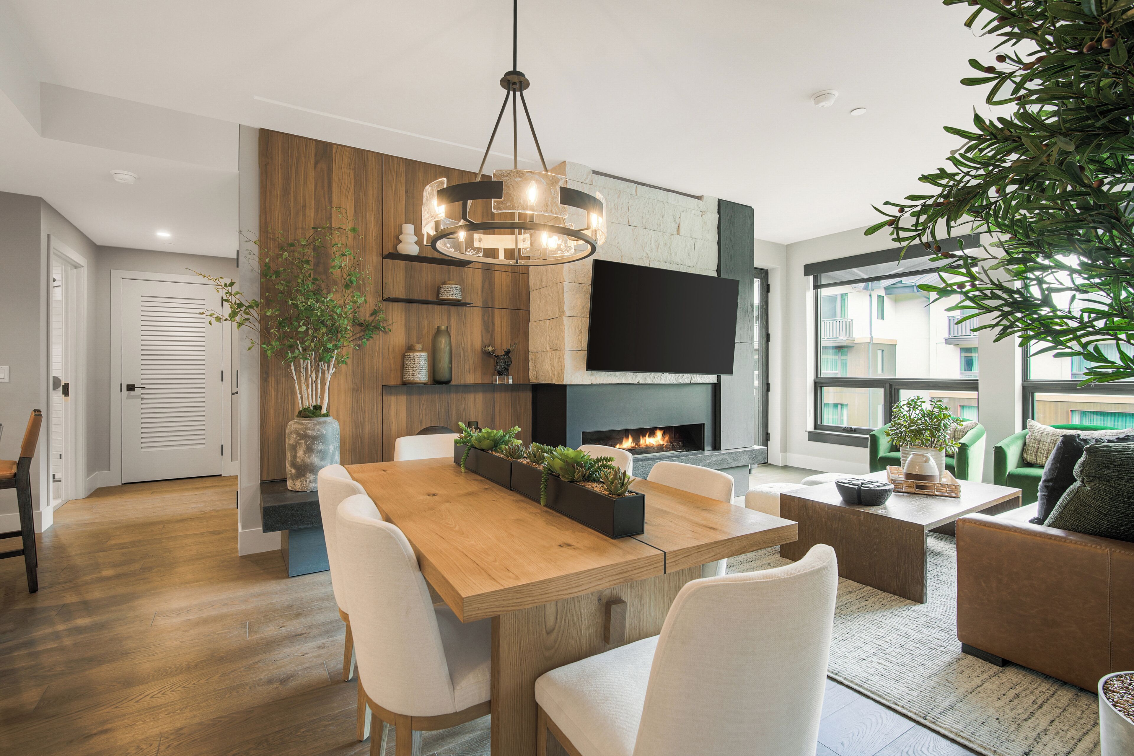 Una sala de estar moderna con una mesa de comedor de madera, sillas blancas, una chimenea, un televisor de pantalla plana y un ventanal grande.