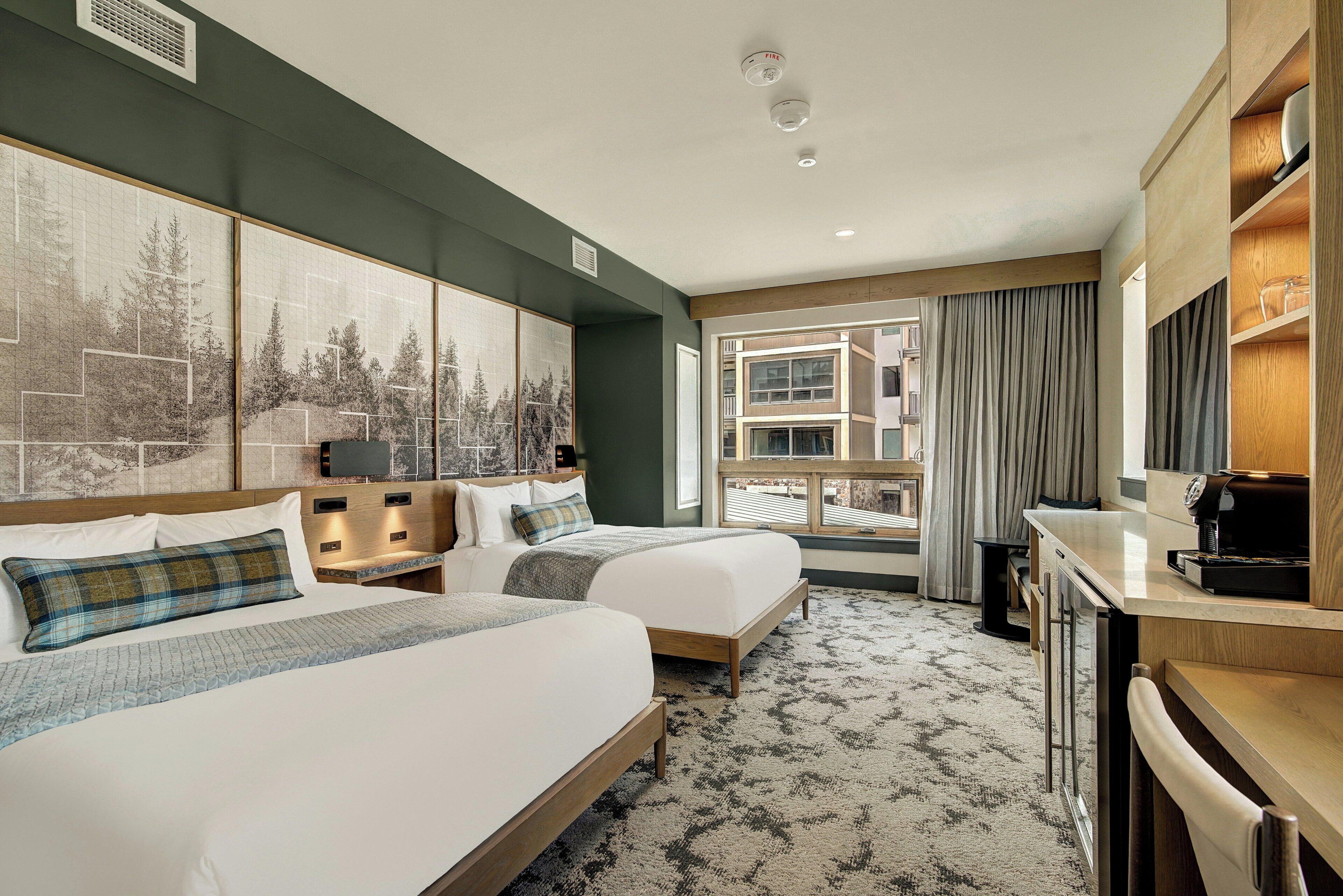 A hotel room with two beds, a desk, a coffee machine, and a large window with curtains.