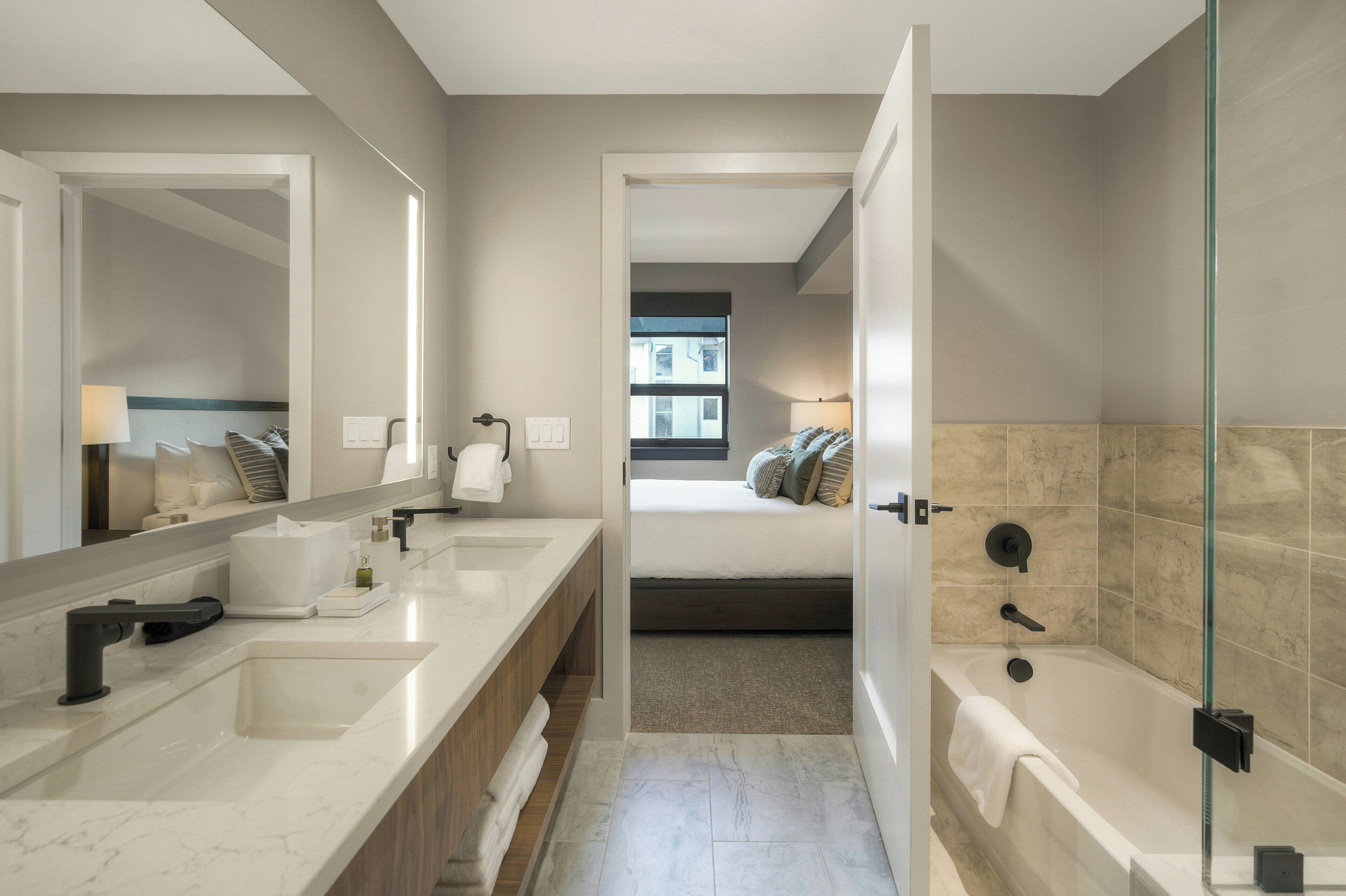 A modern bathroom with a large mirror, dual sinks, a bathtub, and a shower.
