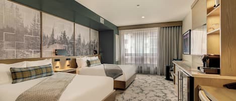 A hotel room with two beds, a desk, a coffee machine, and a large window with curtains.