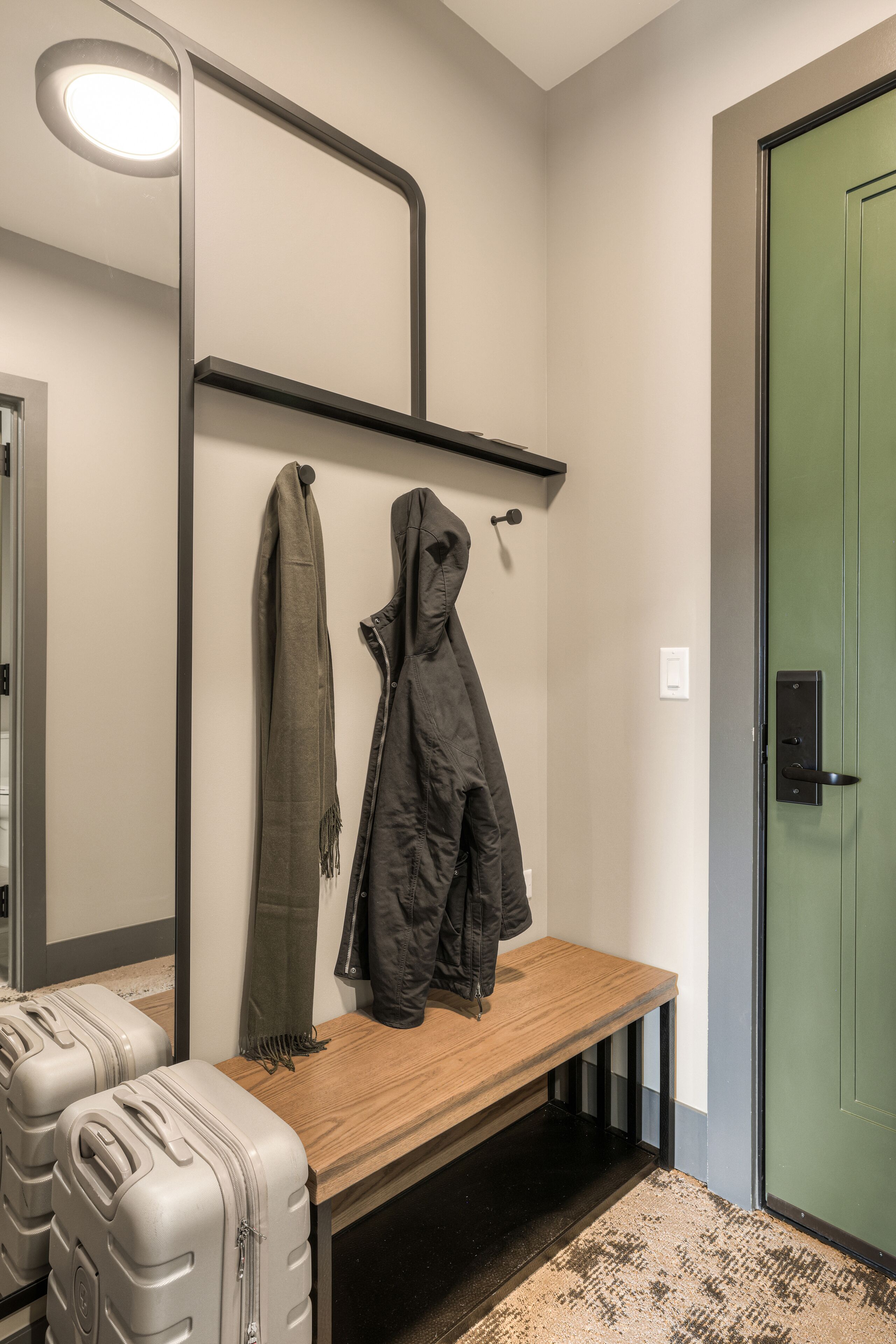 Un banc avec des bagages, un porte-manteau avec un manteau et une écharpe, et une porte verte.