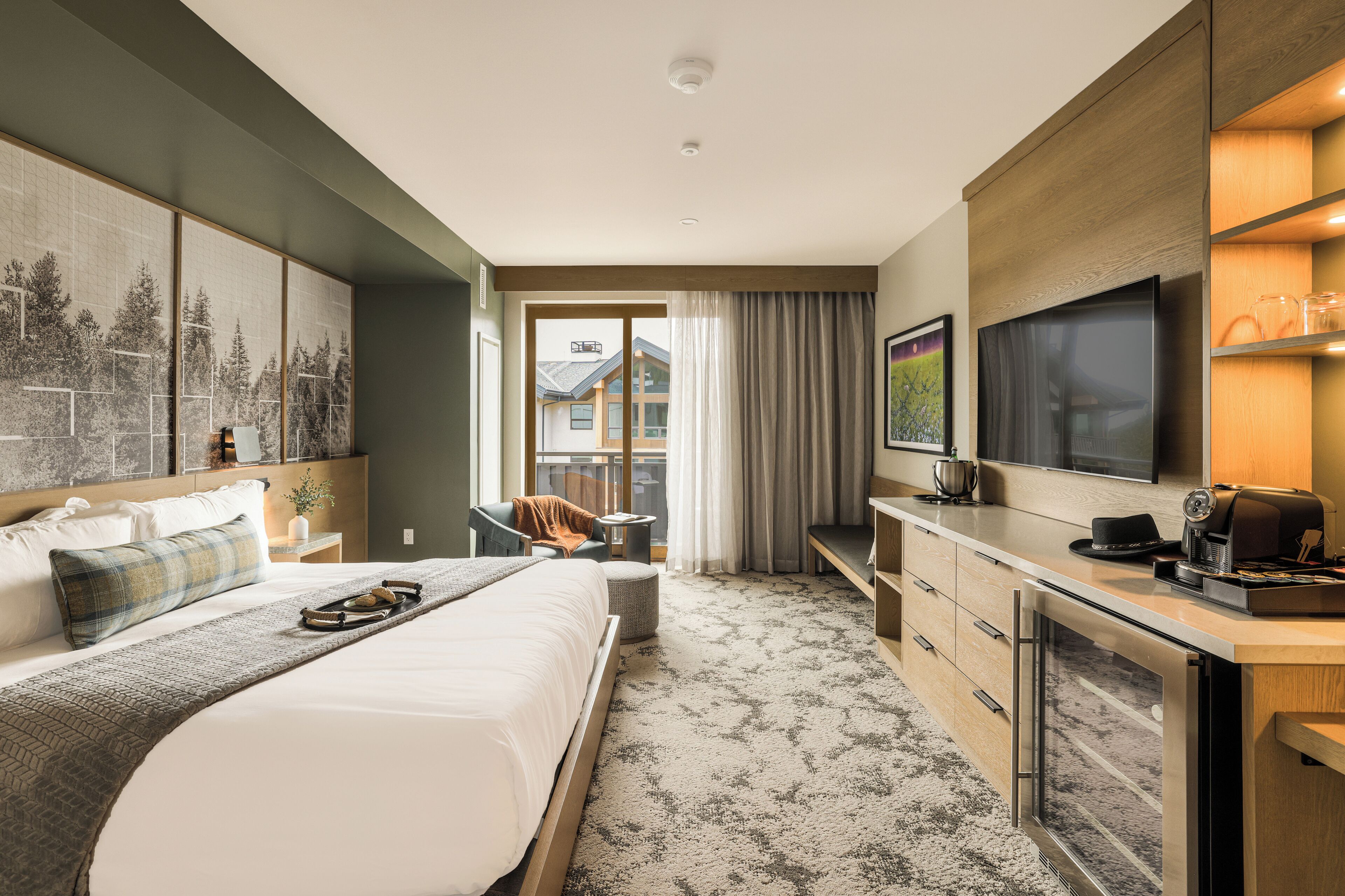 A hotel room with a large bed, a desk, a flat-screen TV, and a view of a building through the window.