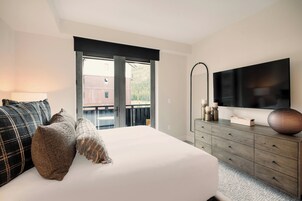 Un dormitorio con cama, cómoda, televisor y balcón con vistas.