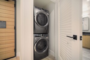 A laundry room with two front-loading washing machines, a wooden door, and a white wall with horizontal lines.