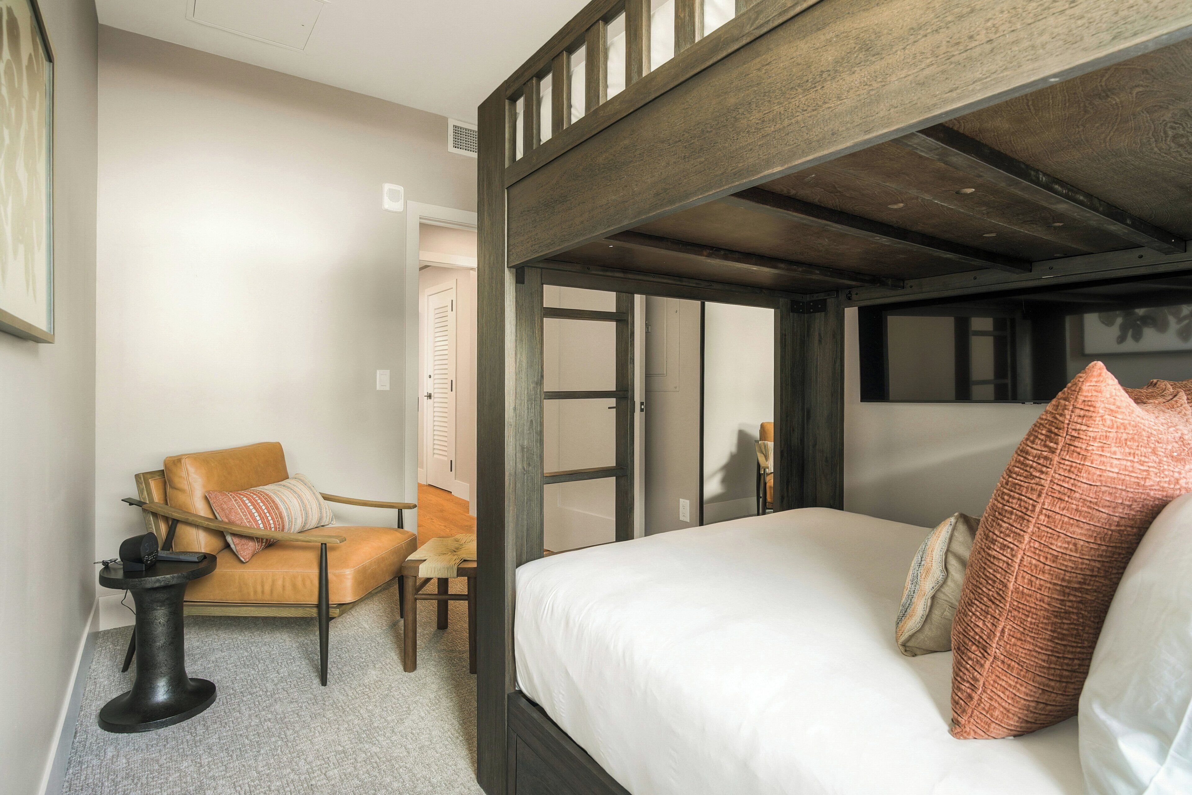 Une chambre à coucher comprenant un lit, une chaise, une table de chevet et une porte donnant sur une autre pièce.