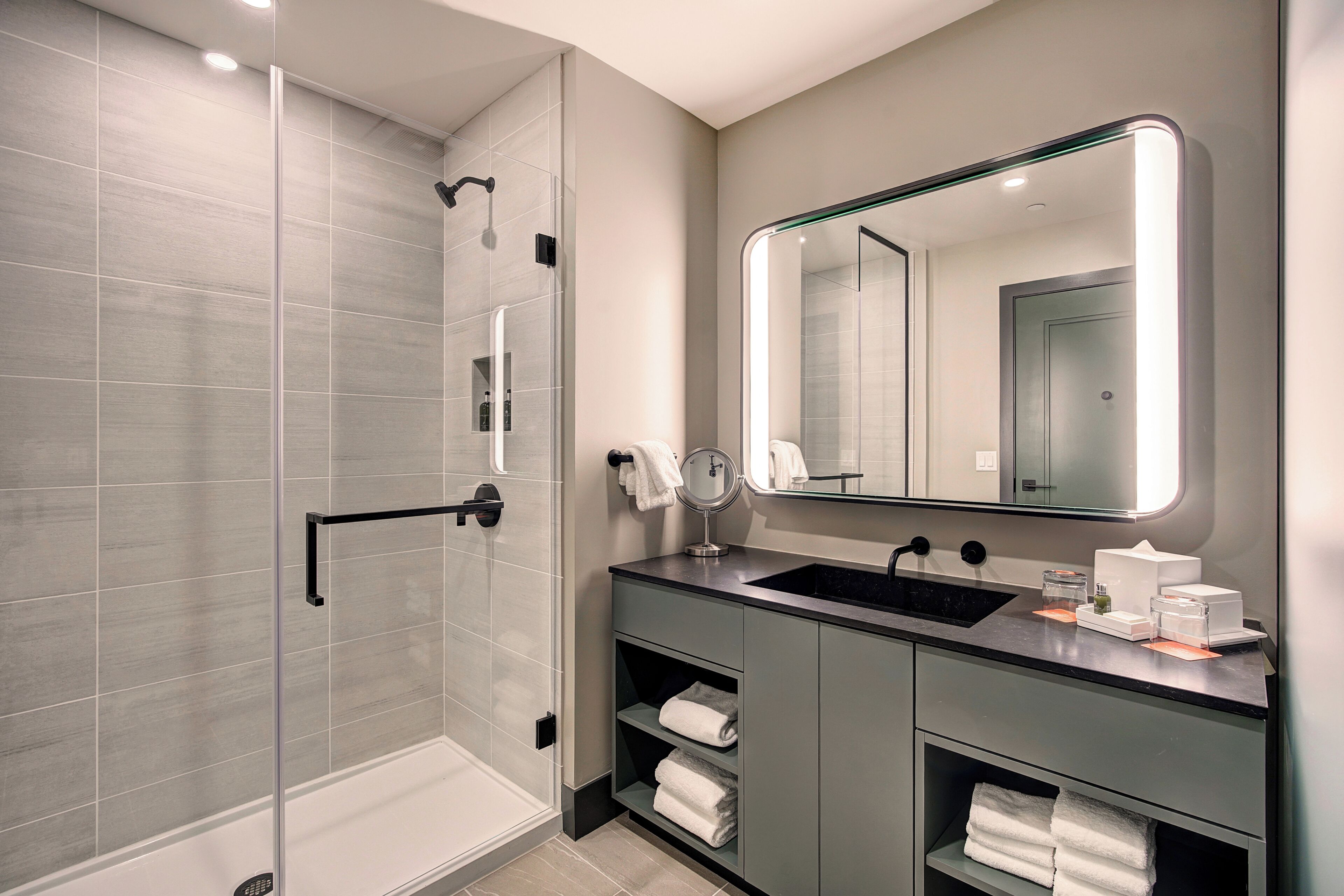 A modern bathroom with a glass-enclosed shower, a large mirror, and a vanity with a sink and towel storage.