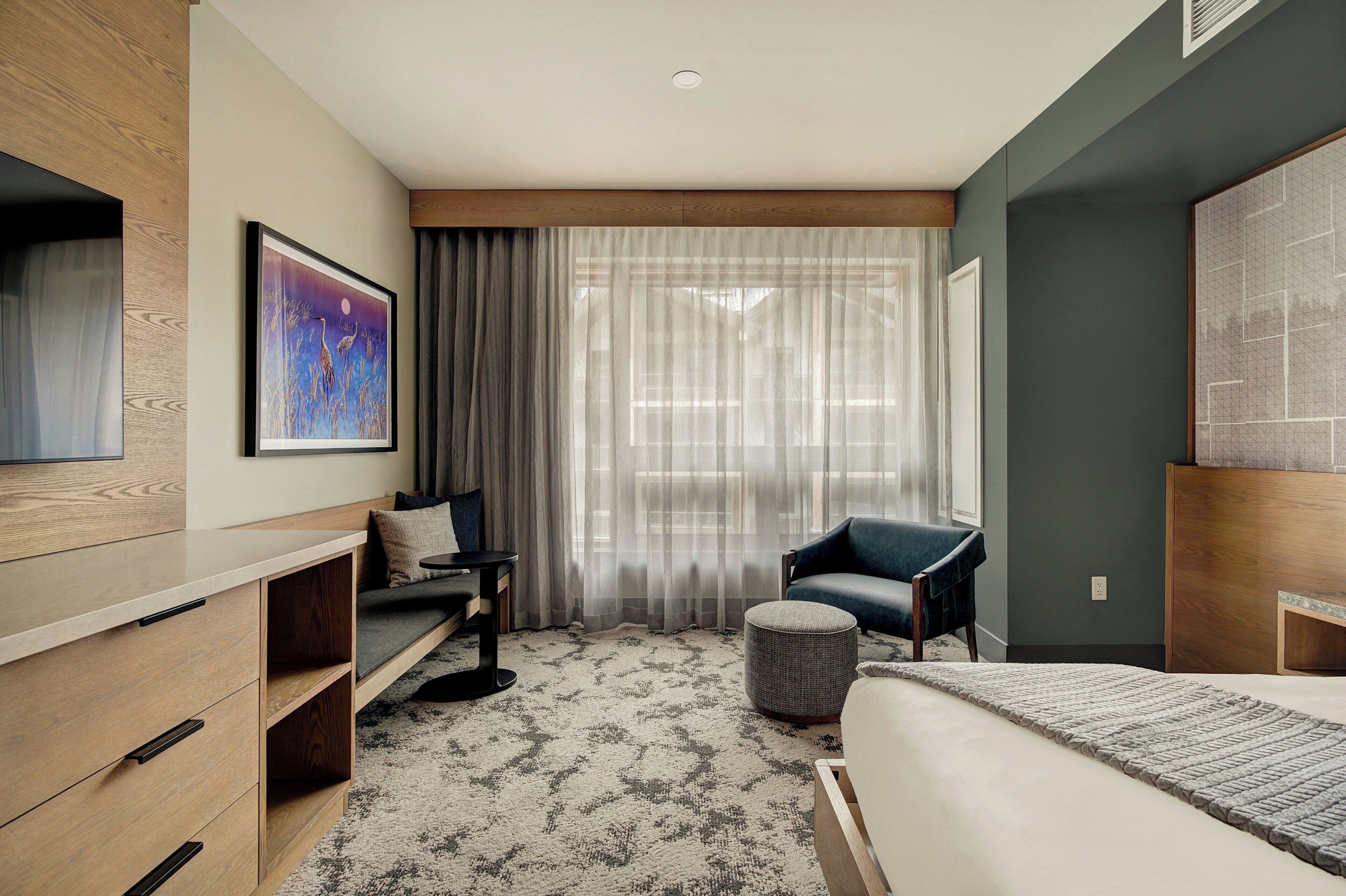 Een moderne hotelkamer met een bed, een sofa, een stoel, een klein tafeltje en een schilderij aan de muur.