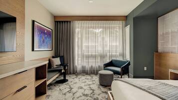 Een moderne hotelkamer met een bed, een sofa, een stoel, een klein tafeltje en een schilderij aan de muur.