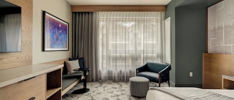 A modern hotel room with a bed, a sofa, a chair, a small table, and a painting on the wall.