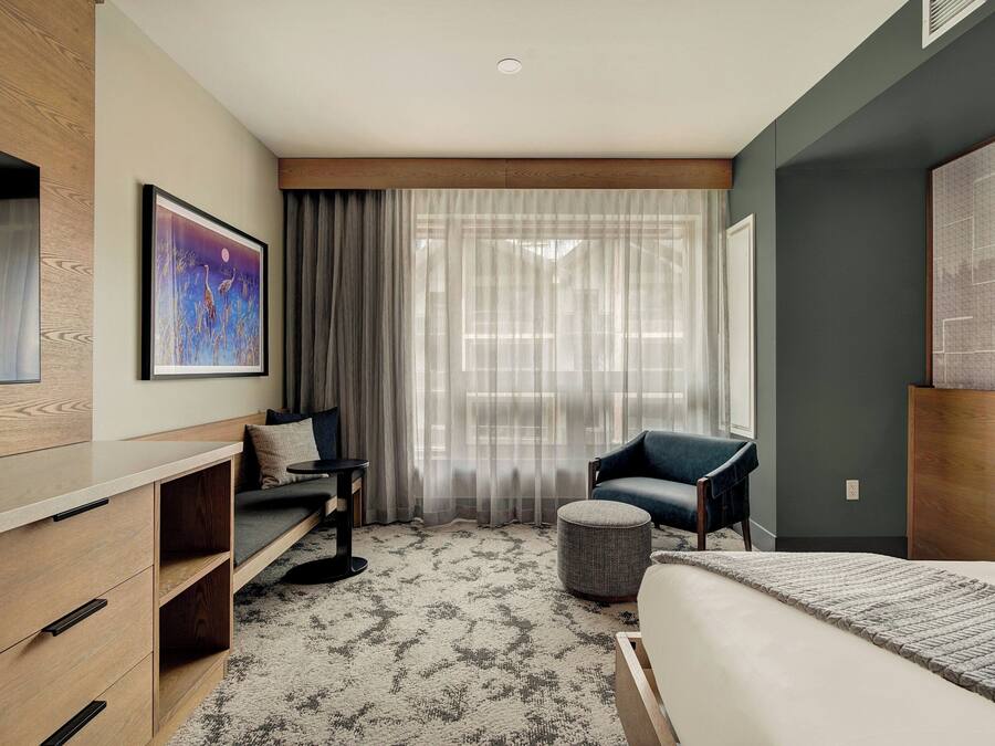 Een moderne hotelkamer met een bed, een sofa, een stoel, een klein tafeltje en een schilderij aan de muur.